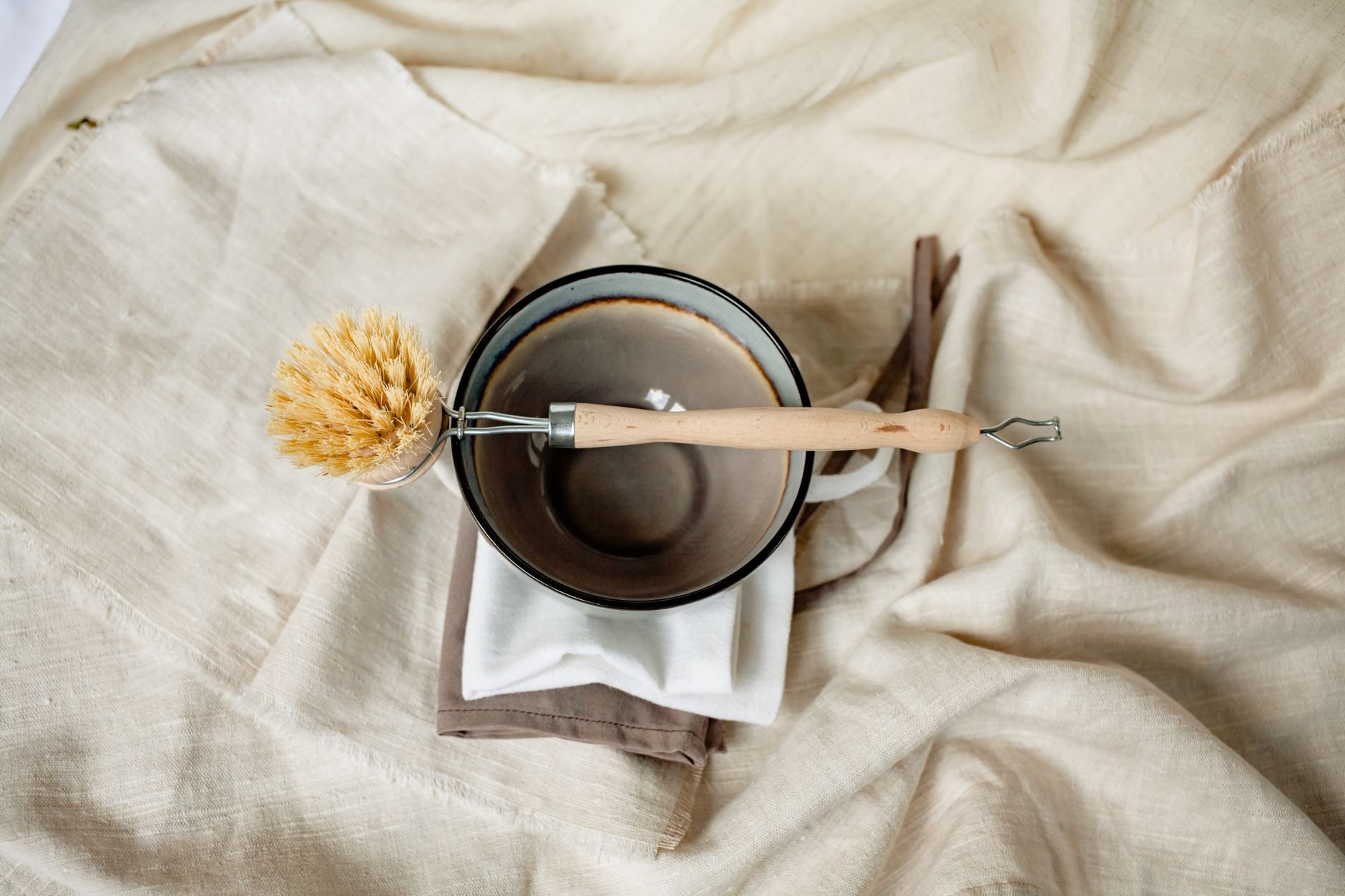 Eco-friendly wooden brush and ceramic bowl on linen fabric — natural home essentials.